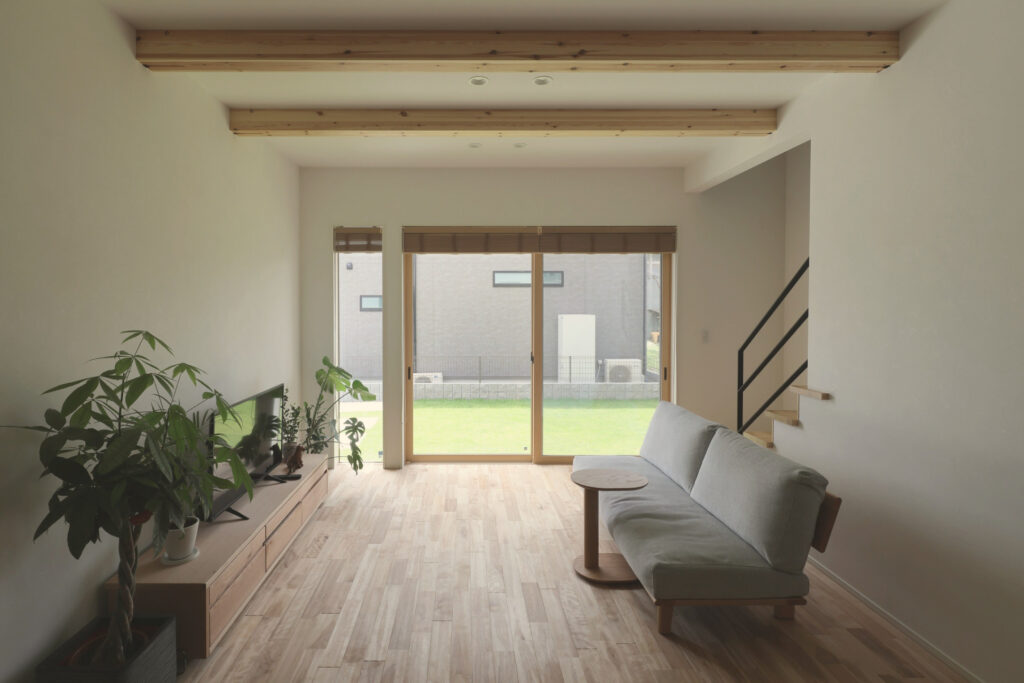 庭の緑が見える、無垢の床と梁のあるシンプルなリビング（丸尾建築の施工事例