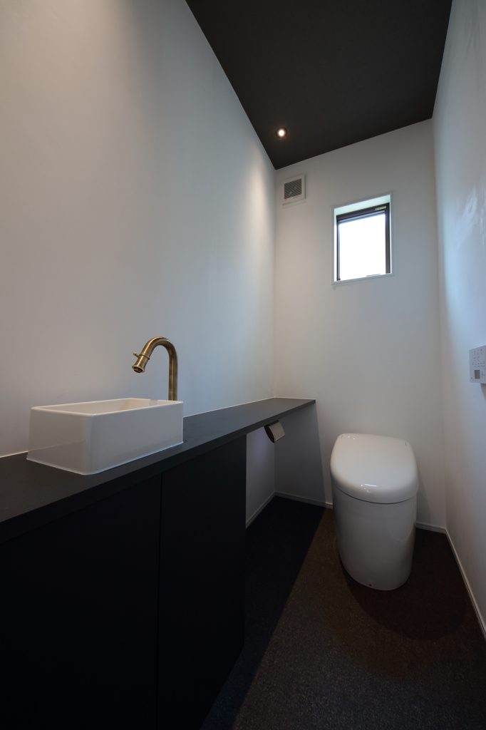 高級感が漂う、黒を基調としたトイレ。造作の手洗いの水栓に真鍮色をアクセントに。